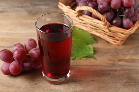 Tasty juice in glass, fresh grapes and leaf on wooden table, closeupの写真素材