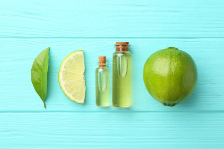 Bottles of essential oils, lime and green leaf on turquoise wooden table, flat layの写真素材