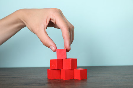 Woman building pyramid of red cubes at wooden table, closeupの写真素材