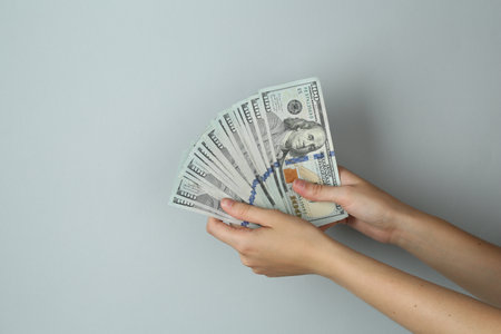 Woman with dollar banknotes on light gray background, closeup. Space for text