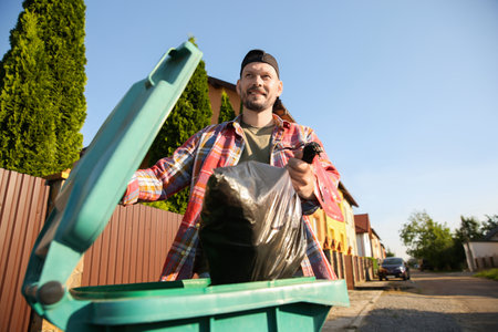 Man throwing trash bag full of garbage into bin outdoors, low angle view. Space for textの写真素材