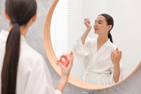 Beautiful woman smelling perfume near mirror in bathroomの写真素材