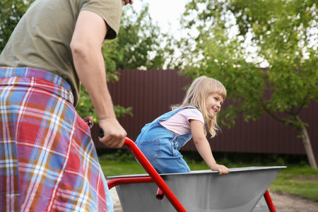 Father pushing wheelbarrow with his daughter outdoors, closeupの写真素材