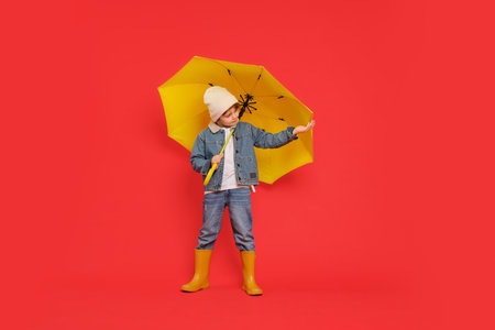 Little boy with yellow umbrella on red backgroundの写真素材