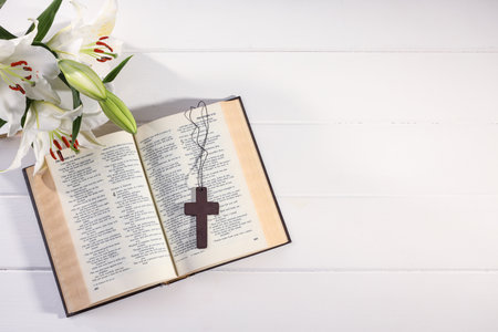 Cross, Bible and beautiful lily flowers on white wooden table, flat lay with space for text....
