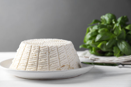 Tasty ricotta (cream cheese), knife and basil on white wooden table, closeupの写真素材