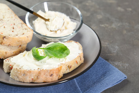 Pieces of bread with cream cheese and basil leaves on gray textured table, closeupの写真素材