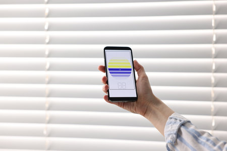 Woman using smartphone to adjust window blinds indoors, closeup. Space for text