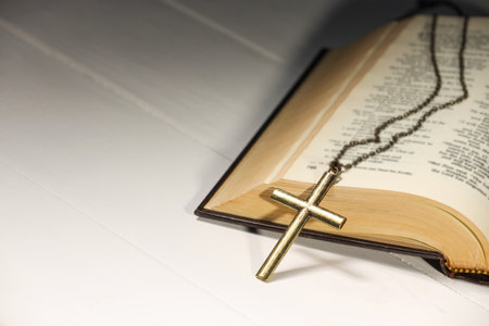 Cross with chain and Bible on white wooden table, closeup with space for text. Religion of...