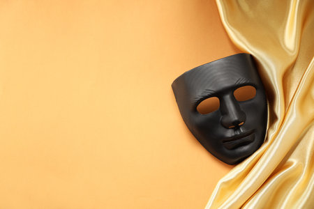 Theater arts. Black mask and golden fabric on pale orange background, top view. Space for textの写真素材