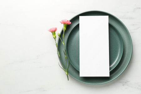 Empty menu, plates and floral decor on white marble table, top view. Mockup for designの写真素材