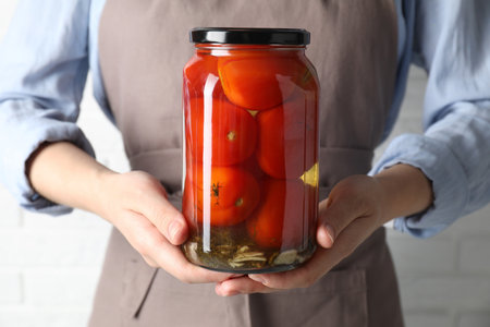 Woman holding jar with tasty pickled tomatoes on light background, closeupの写真素材