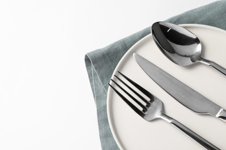 Stylish silver cutlery, plate and napkin on white background, top view. Space for text