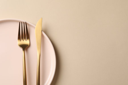 Stylish golden cutlery and plate on beige background, top view. Space for textの写真素材