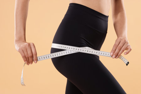 Diet and weight loss concept. Woman with measuring tape showing her slim body against beige...