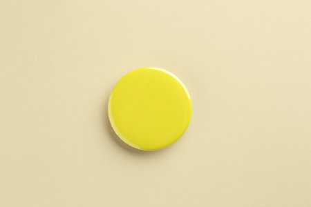Yellow button badge on beige background, top view. Mockup for designの写真素材