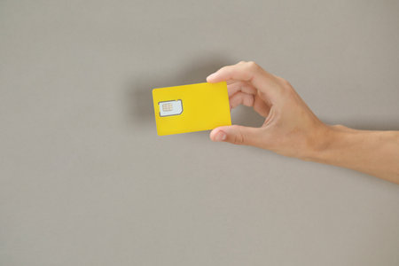 Man holding SIM card on gray background, closeup
