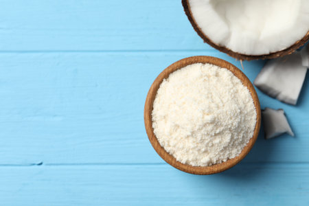 Fresh coconut flour in bowl and nut on light blue wooden table, top view. Space for text