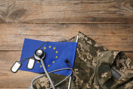 Stethoscope, flag of European Union, tags and military uniform on wooden table, flat lay. Space for textの写真素材