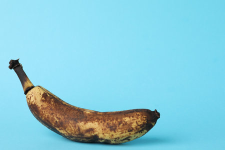 Overripe banana with dark spots on light blue background. Space for textの写真素材