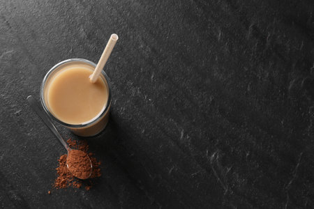 Delicious protein shake in glass and spoon with powder on black table, top view. Space for textの写真素材