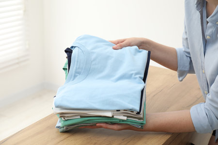 Woman stacking clean clothes at wooden table indoors, closeupの写真素材