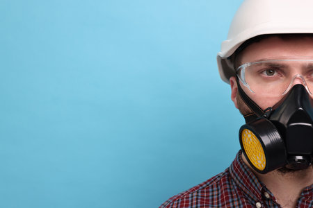 Man in respirator mask and hard hat on light blue background. Space for textの写真素材