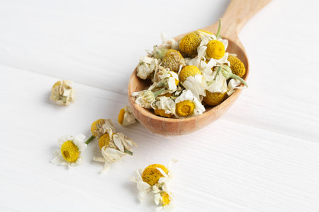Chamomile flowers in spoon on white wooden tableの写真素材