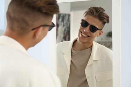 Handsome man in glasses looking at mirror indoorsの写真素材