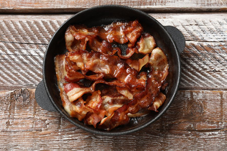 Delicious bacon slices in frying pan on wooden table, top viewの写真素材