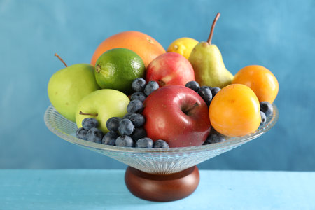 Glass vase with different fresh fruits on light blue wooden table, closeupの写真素材