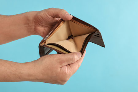 Man with empty wallet on light blue background, closeup. Space for textの写真素材