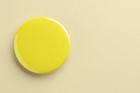 Yellow button badge on beige background, top view. Mockup for designの写真素材