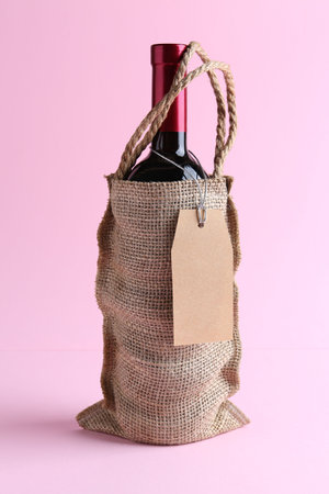 Wine bottle in burlap bag on pink backgroundの写真素材