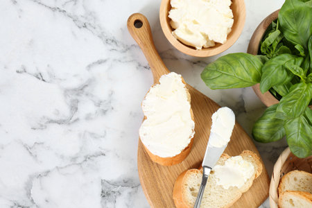 Pieces of bread with cream cheese and basil served on white marble table, flat lay. Space for textの写真素材