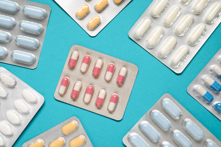 Antibiotic pills in blisters on light blue background, flat lay