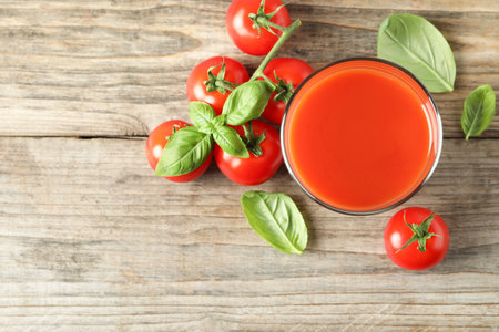 Tasty tomato juice in glass, basil leaves and fresh vegetables on wooden table, flat lay. Space for textの写真素材