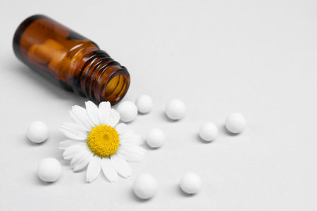 Homeopathy. Overturned glass bottle, pills and chamomile on white backgroundの写真素材
