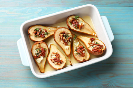 Delicious baked pears with nuts, blue cheese, thyme and honey in baking dish on light blue wooden table, top viewの写真素材