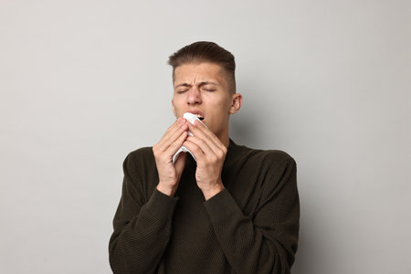 Sick man with tissue suffering from cold symptoms on light grey backgroundの写真素材