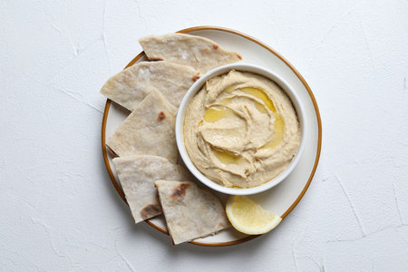 Delicious hummus with olive oil in bowl and pita on light textured table, top view