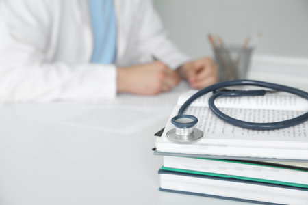 Doctor at white table in hospital, focus on medical stethoscope and booksの写真素材