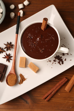 Tasty melted chocolate in cup, marshmallows, candies and spices on wooden table, flat lay