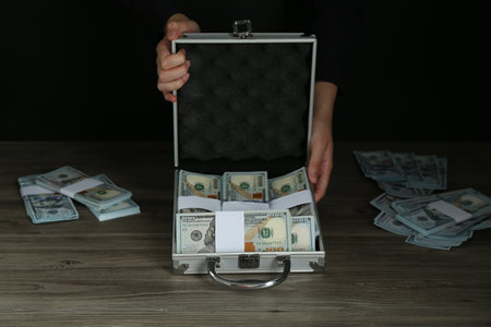 Woman with metal case full of dollar banknotes at wooden table, closeupの写真素材