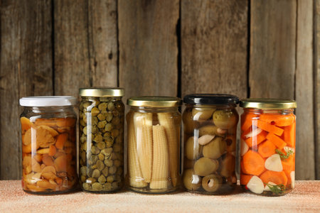 Different pickled products in jars on beige textured tableの写真素材