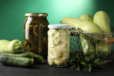 Different pickled products in jars and fresh ingredients on black wooden tableの写真素材