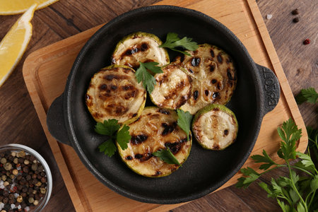 Tasty grilled zucchini slices with parsley in dish served on wooden table, flat layの写真素材