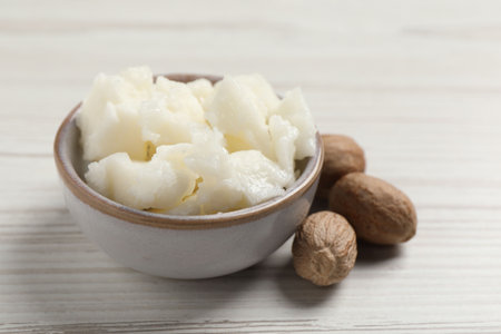 Shea butter in bowl and nuts on white wooden table, closeupの写真素材