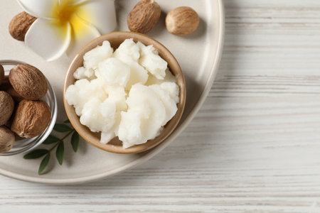 Shea butter in bowl, flower and nuts on white wooden table, top view. Space for textの写真素材