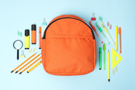 Orange backpack and different school supplies on light blue background, flat layの写真素材